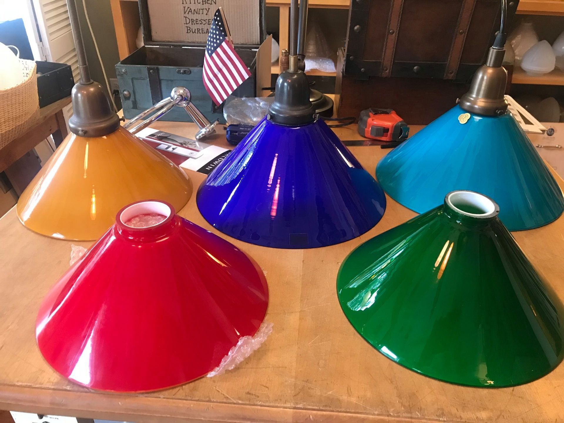 Five colorful, cone-shaped glass lampshades: yellow, blue, turquoise, green, and red, on a wooden table.