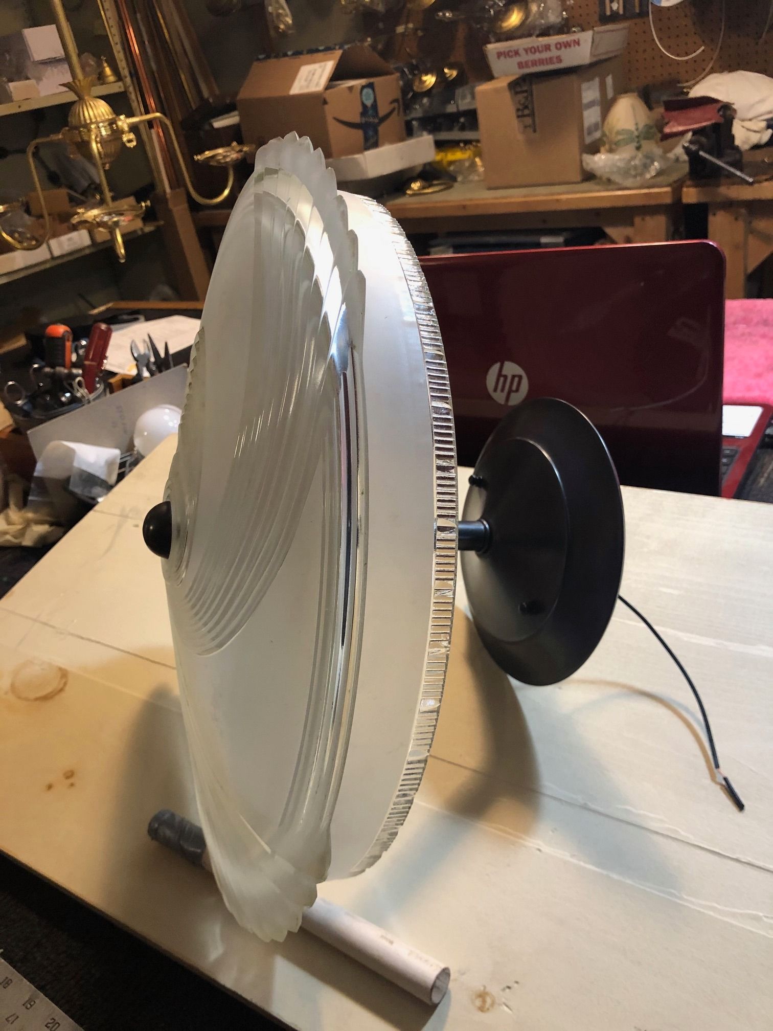 Round frosted glass light fixture, black bracket, sitting on a wooden surface, with a laptop in the background.