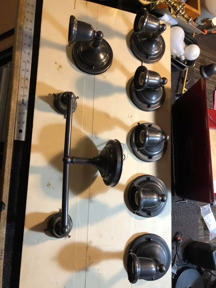 Dark bronze vintage wall sconces and a dual-arm light fixture laid on a light-colored wooden surface.