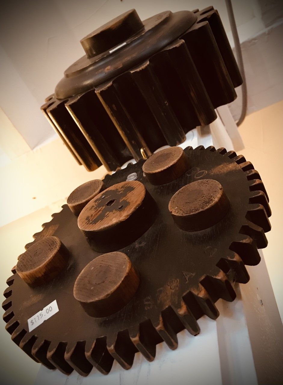 Two large, dark metal gears meshing together. One gear has pegs on top.