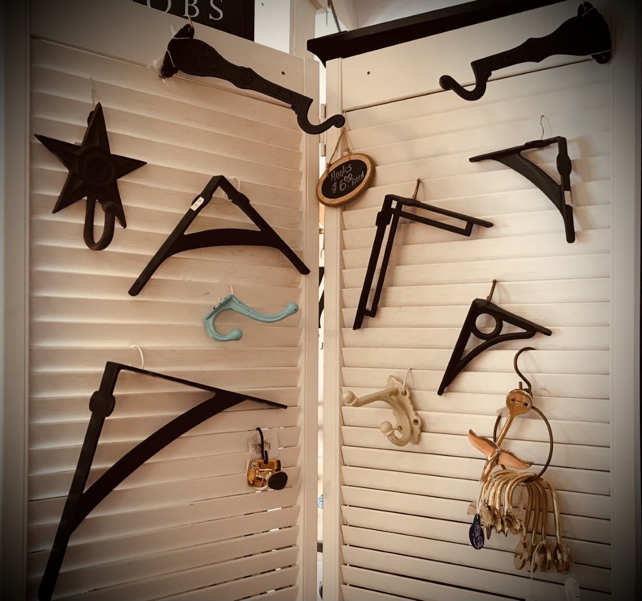 Black metal decorative brackets, hooks, and star hanging on a white shuttered background.