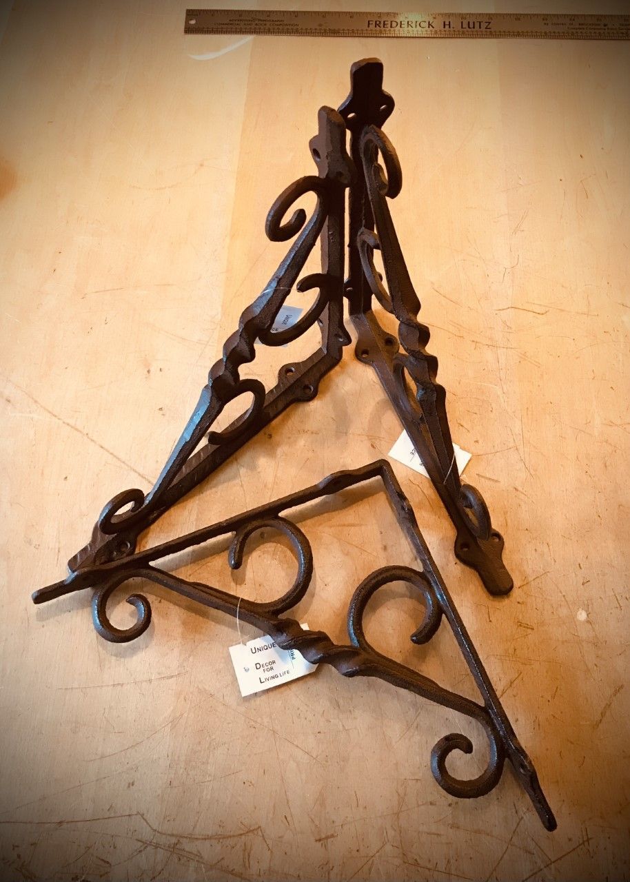 Two decorative, rusty metal brackets. One is standing, the other lying down, both on a beige surface.