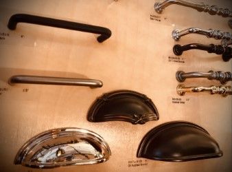 Cabinet hardware samples: various drawer pulls and handles in different styles and finishes displayed on a wooden board.