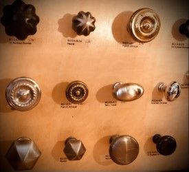 Assortment of antique door knobs, varying shapes and finishes, displayed on a wooden panel.