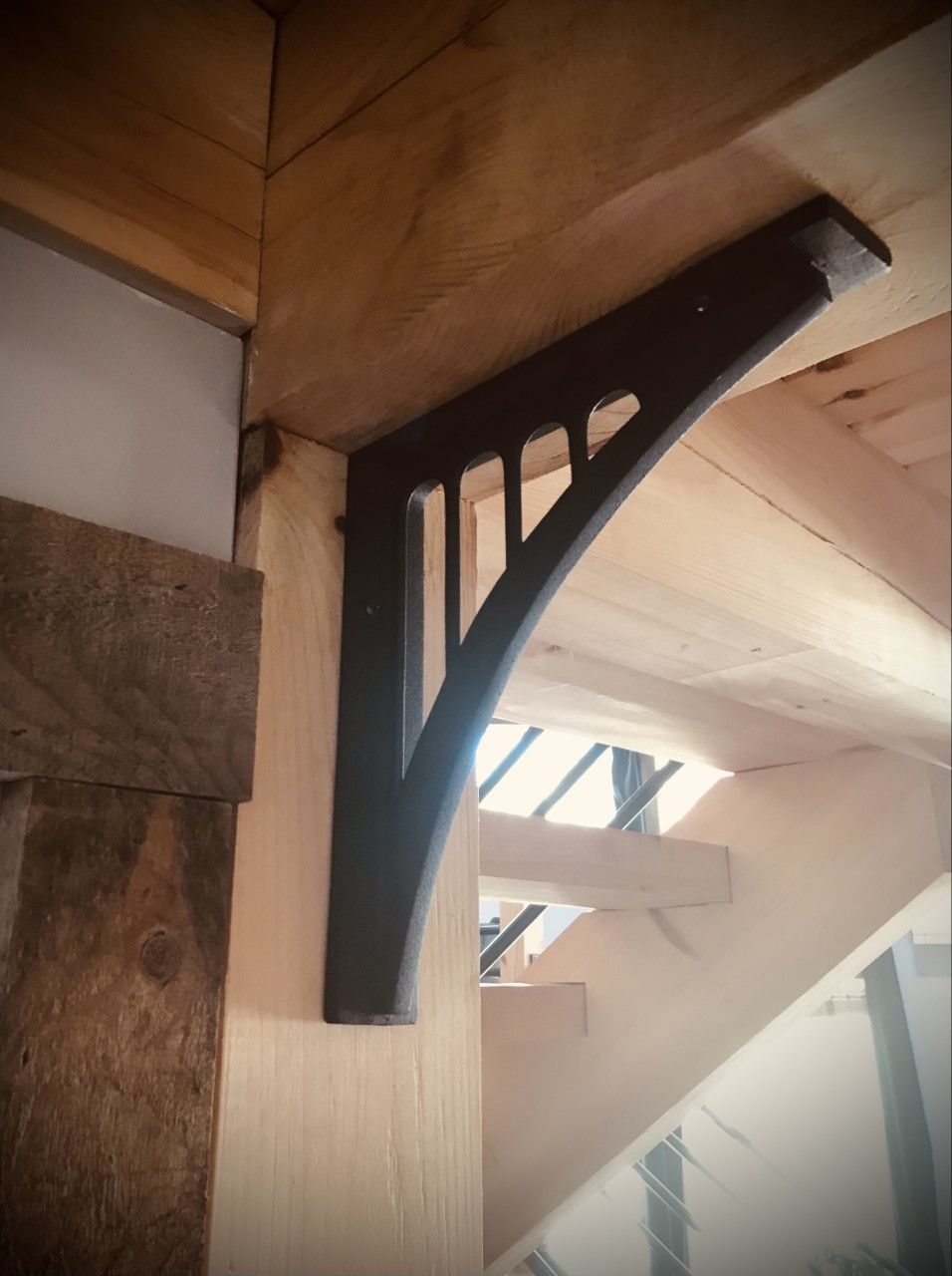 Dark bracket supporting a wooden beam. Interior view with stairs in the background.