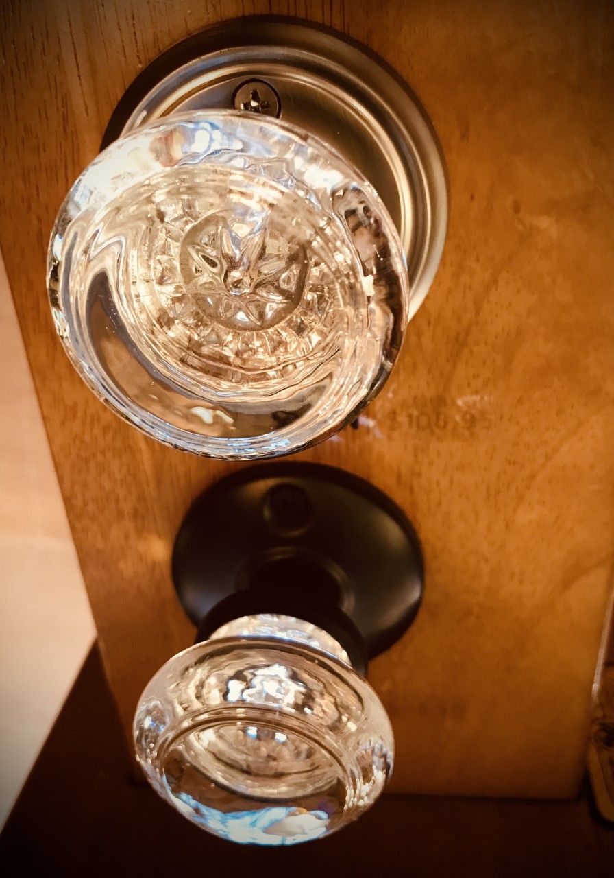Clear glass doorknobs on wooden door, one silver, one black plate.
