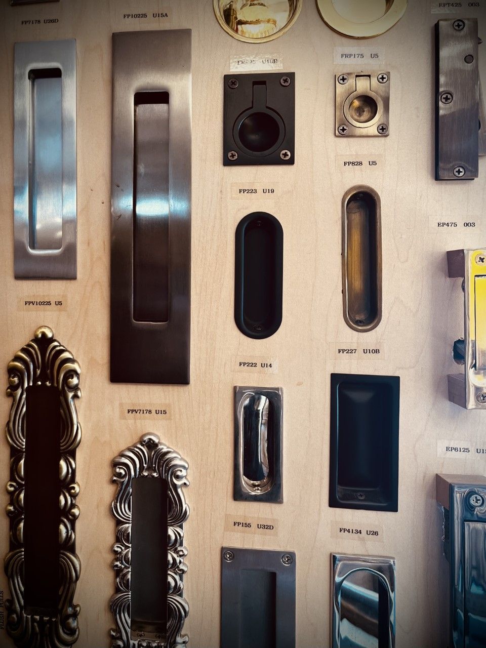 Display of various metal door handles and pulls on a wooden board.