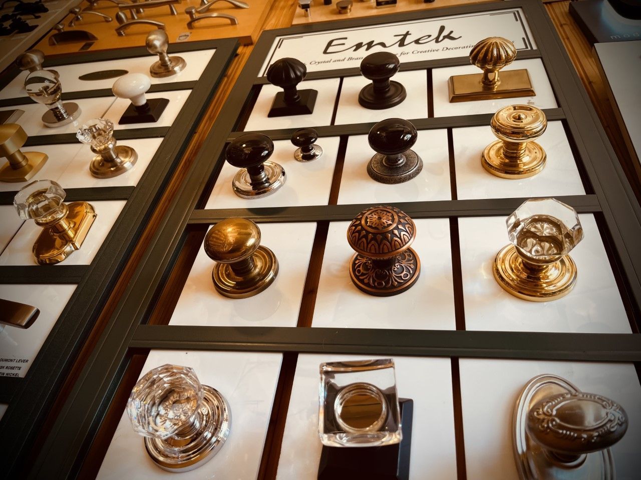 Display of various Emtek doorknobs on white backgrounds within a display case.