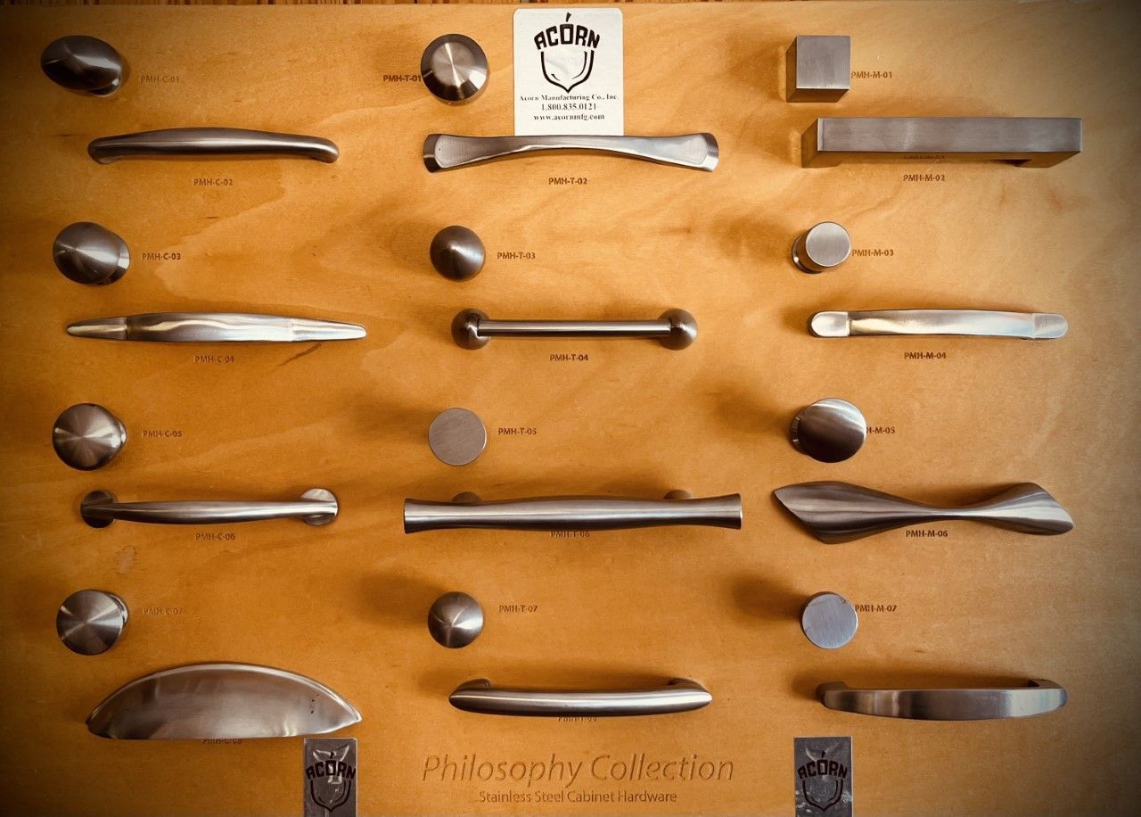 Display board with various metal cabinet pulls and knobs, arranged on a wood background.