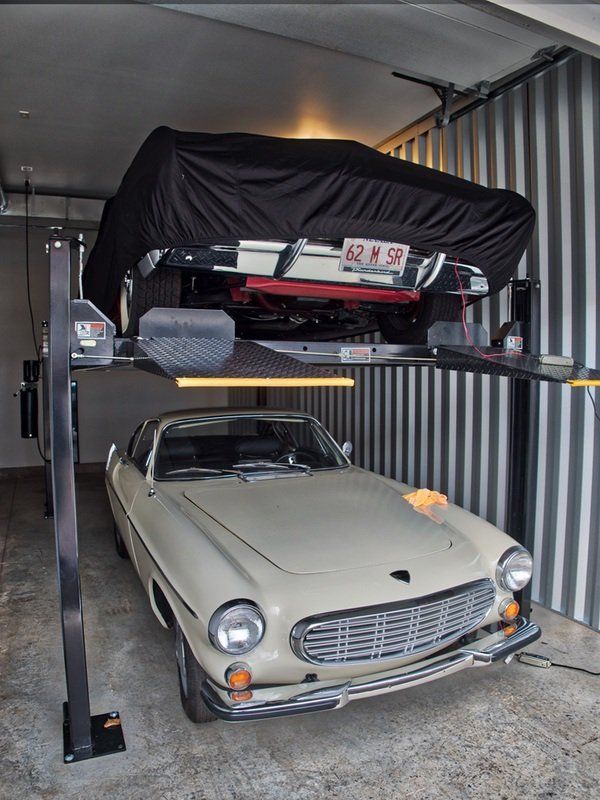 Image of a luxury car storage bay containing two cars - one on a lift, the other below