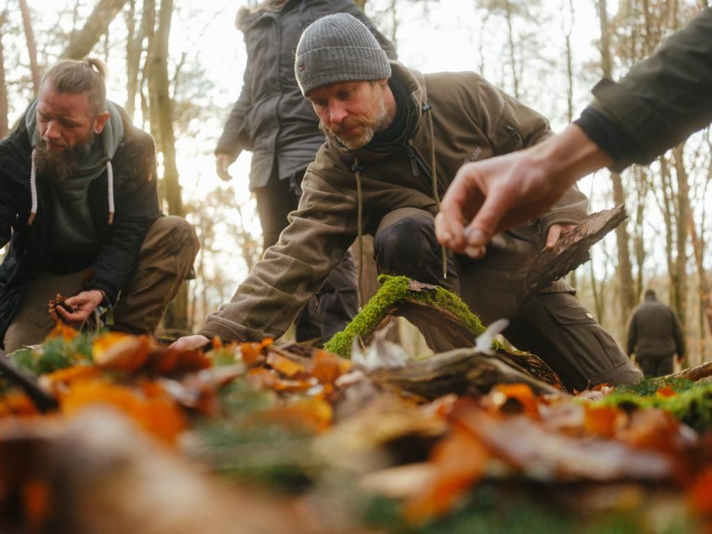 Ein Wanderer in einer neonfarbenen Jacke und mit einem großen Rucksack geht durch einen nebligen Wald auf andere Personen zu, die sich in der Nähe eines kleinen weißen Zeltes befinden.