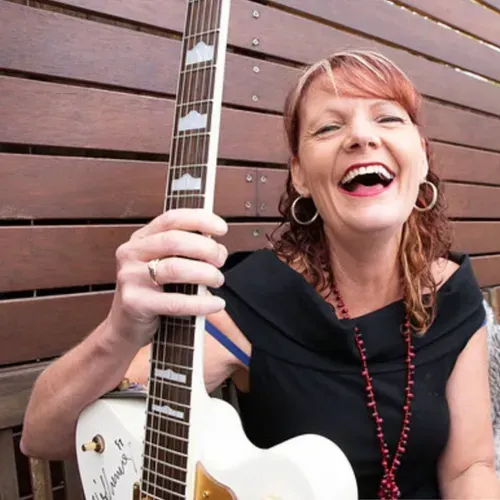 A Woman in a Black Dress is Holding a White Guitar and Smiling — Chop 'n Chill South West Rocks in South West Rocks, NSW