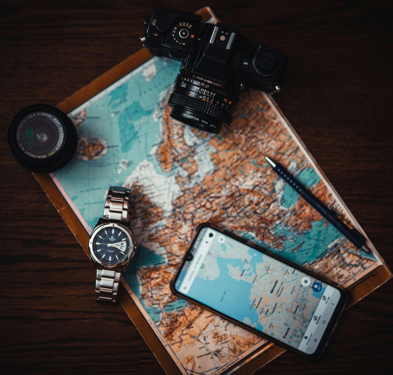 A watch , a cell phone , a camera , and a pen are sitting on top of a map.