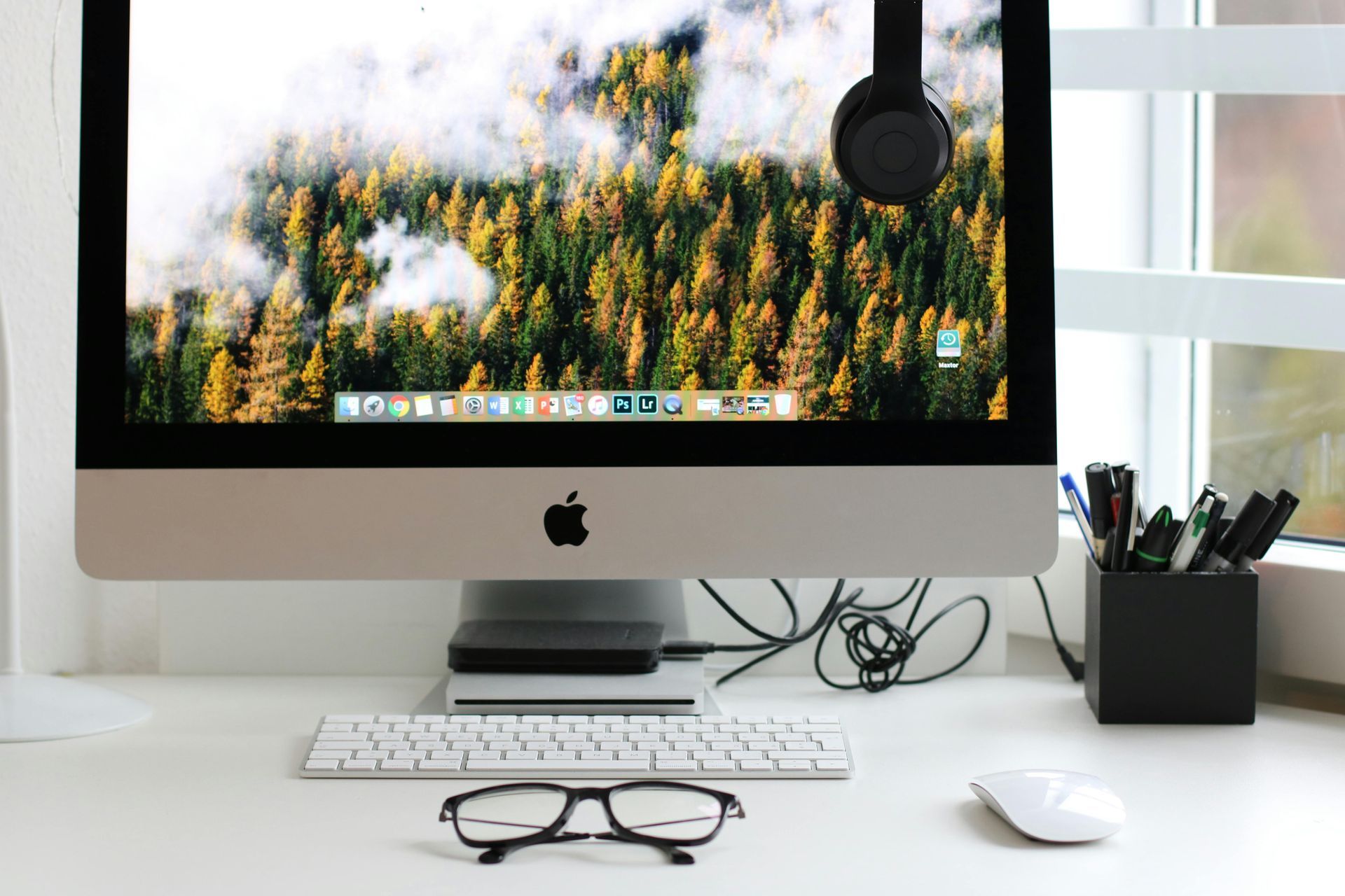 An apple computer is sitting on a desk next to a window.