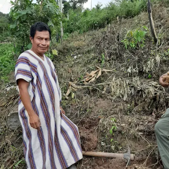 Un homme en robe rayée se tient debout dans la terre à côté d'une pelle.