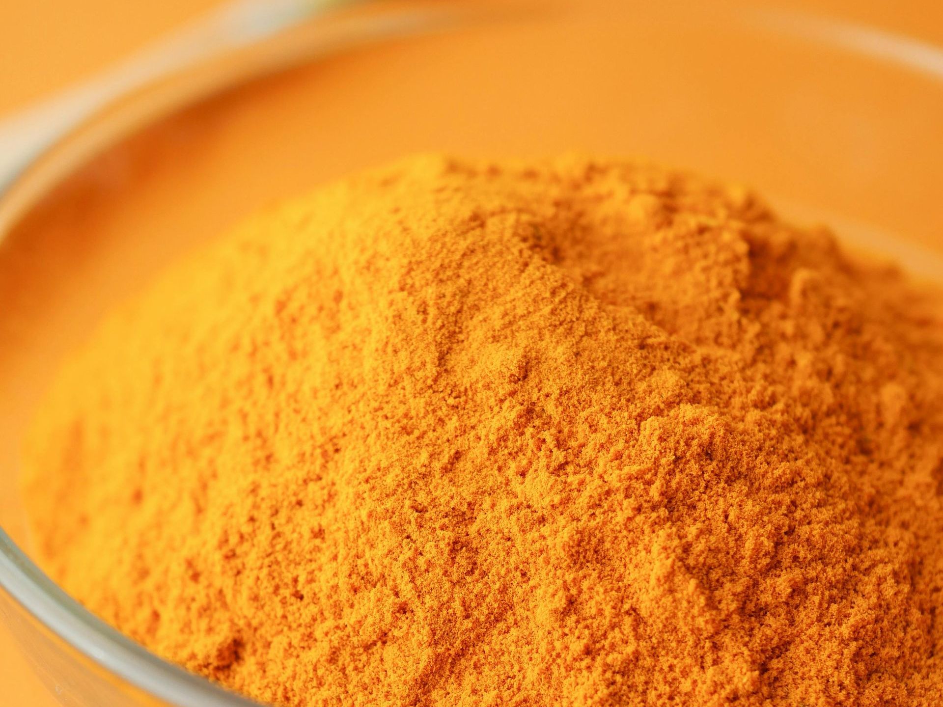 Un gros plan d'un bol de poudre de curcuma sur fond orange.