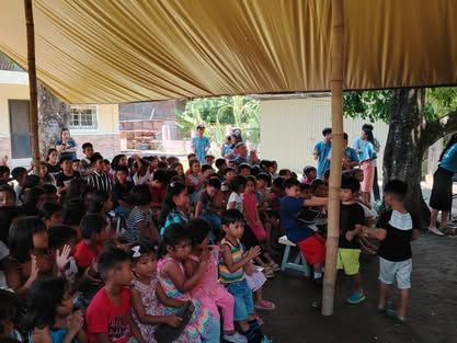 A large group of children are sitting under a tent.