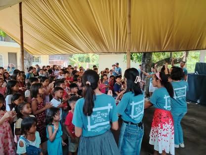 A group of people are standing in front of a crowd of children.