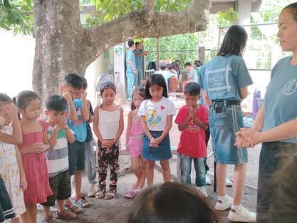 A group of children are standing in a circle under a tree.