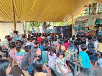 A large group of children are sitting under a tent.