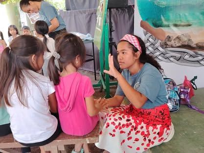 A girl is sitting on a bench talking to a group of children.