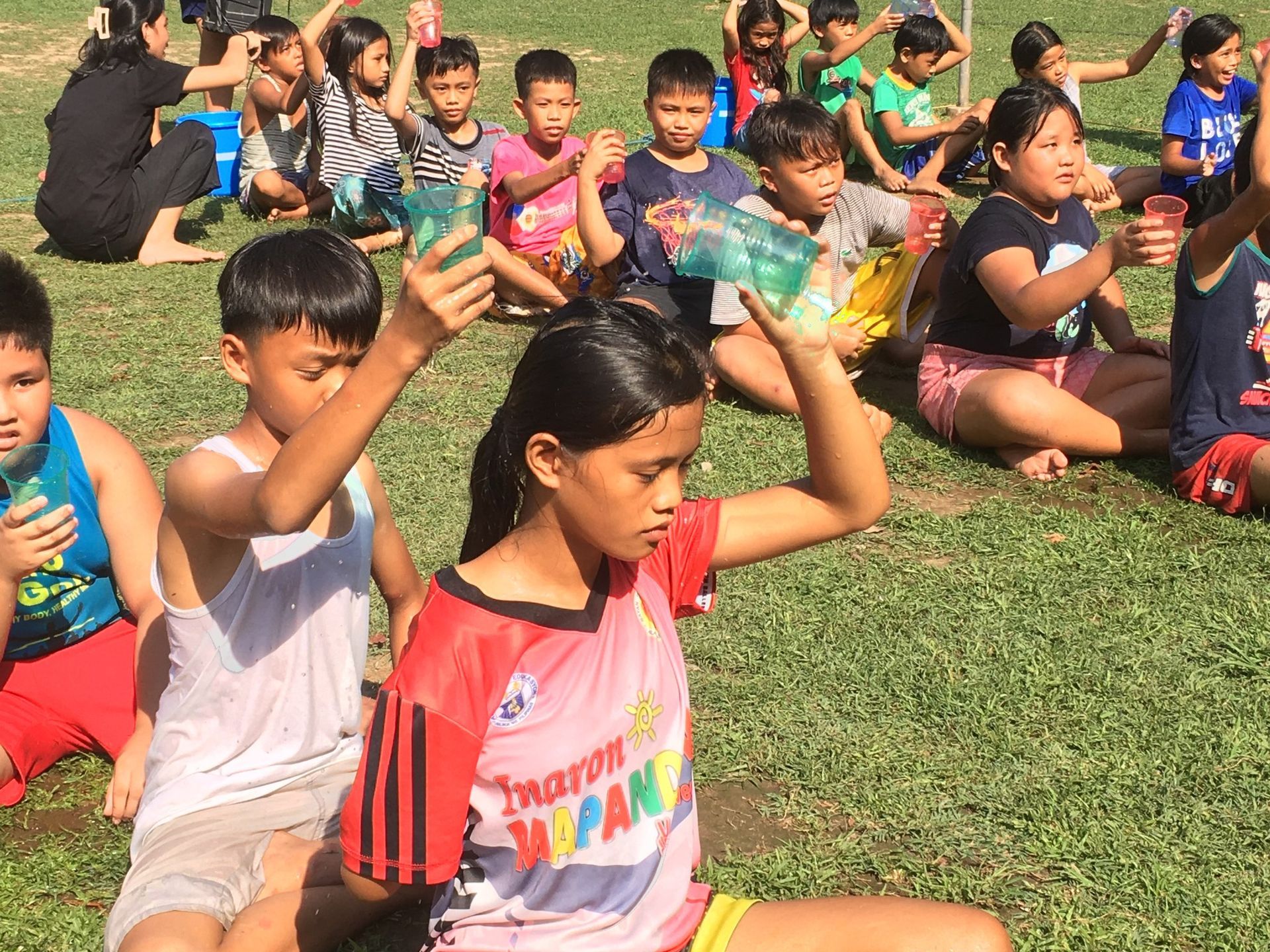 A group of children are sitting on the grass holding bottles of water.
