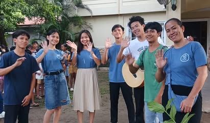 A group of young people are standing next to each other and waving at the camera.