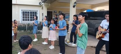 A group of children are singing and playing guitars in front of a house.
