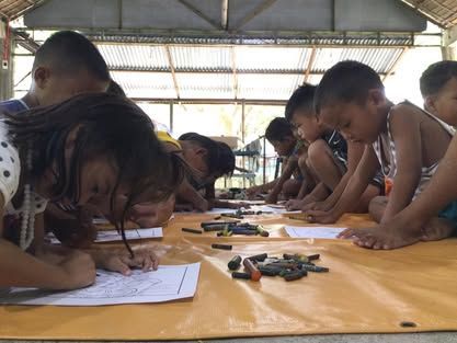A group of children are sitting on the floor drawing with crayons.