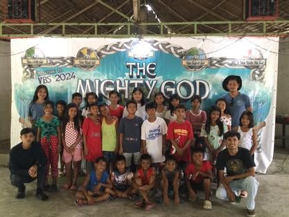 A group of children are posing for a picture in front of a sign that says the mighty god.