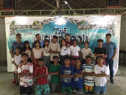 A group of young people are posing for a picture in front of a sign.
