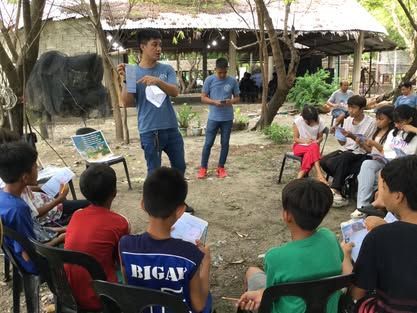 A man is standing in front of a group of children sitting in chairs.