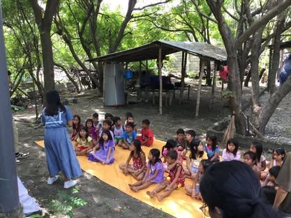 A group of children are sitting on a yellow mat in the woods.