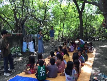 A group of children are sitting on a mat in the woods.