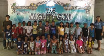 A group of children are posing for a picture in front of a sign that says `` the mighty god ''.