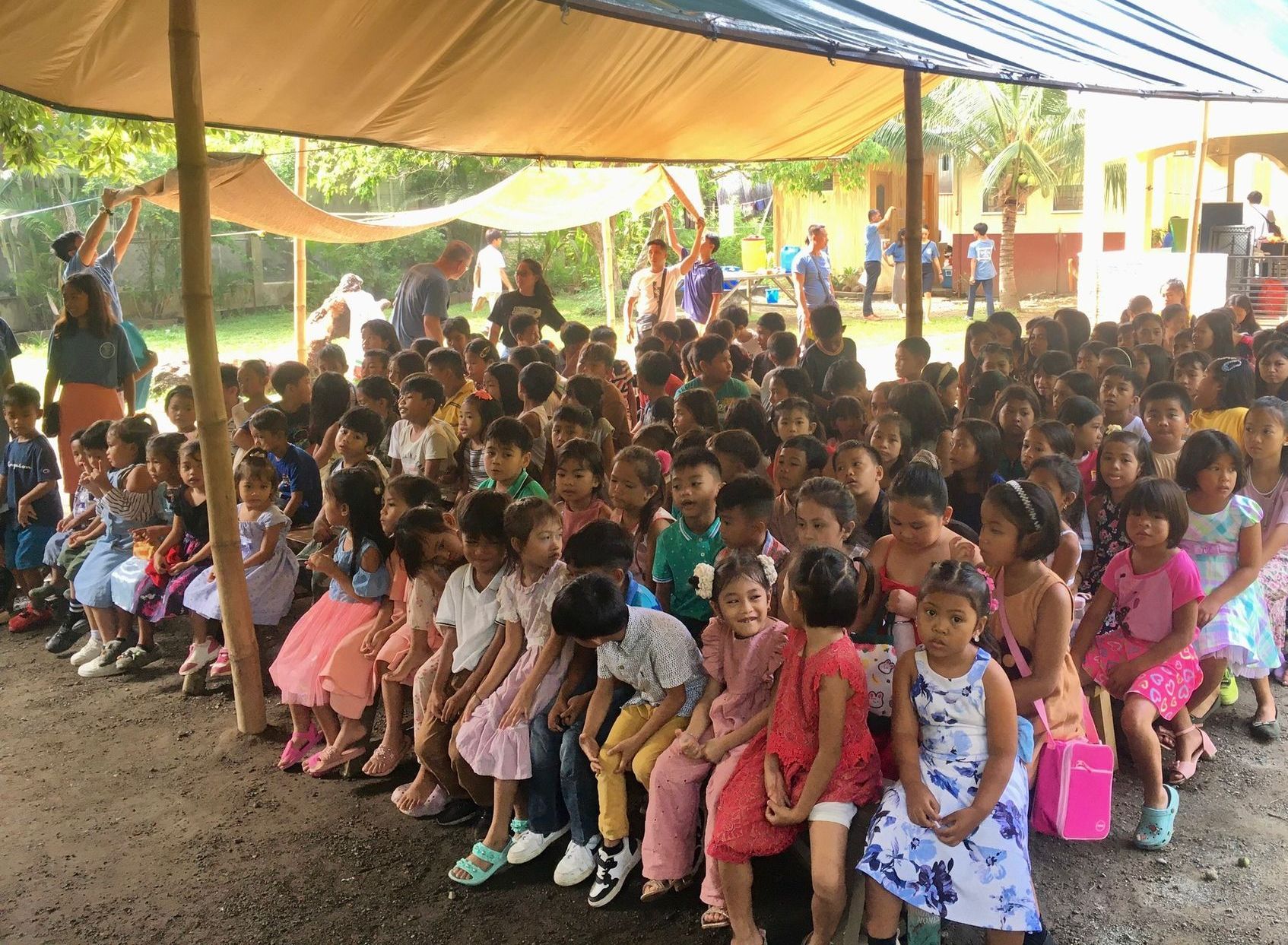A large group of children are sitting under a tent.