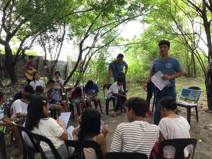 A group of people are sitting in a circle under trees.