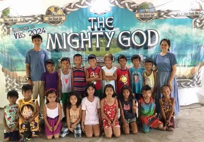 A group of children are posing for a picture in front of a sign that says the mighty god.