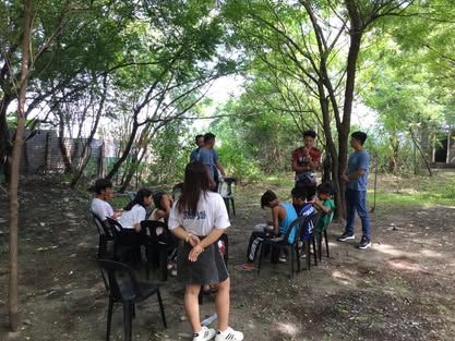 A group of people are sitting in chairs under trees.