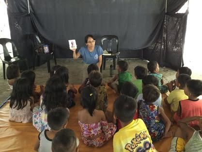 A woman is reading a book to a group of children sitting on the floor.