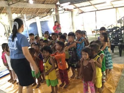 A woman is standing in front of a group of children.