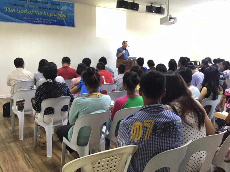 A man is giving a speech to a large group of people sitting in chairs.