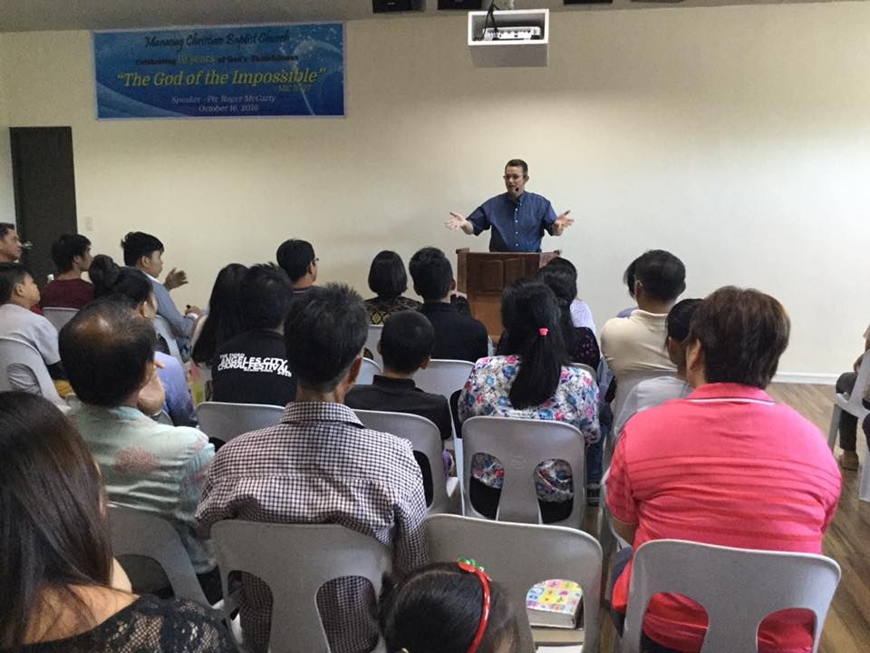 A man is giving a speech to a group of people sitting in chairs.