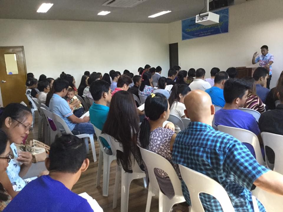 A large group of people are sitting in chairs in a room watching a presentation.