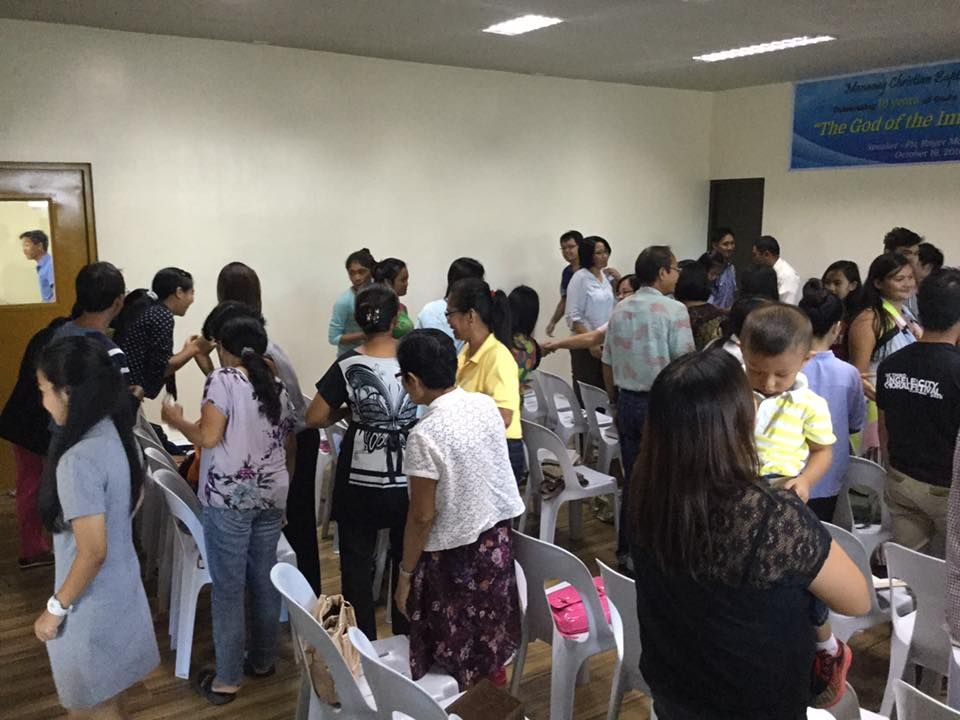 A group of people are standing in a room with a sign on the wall that says service