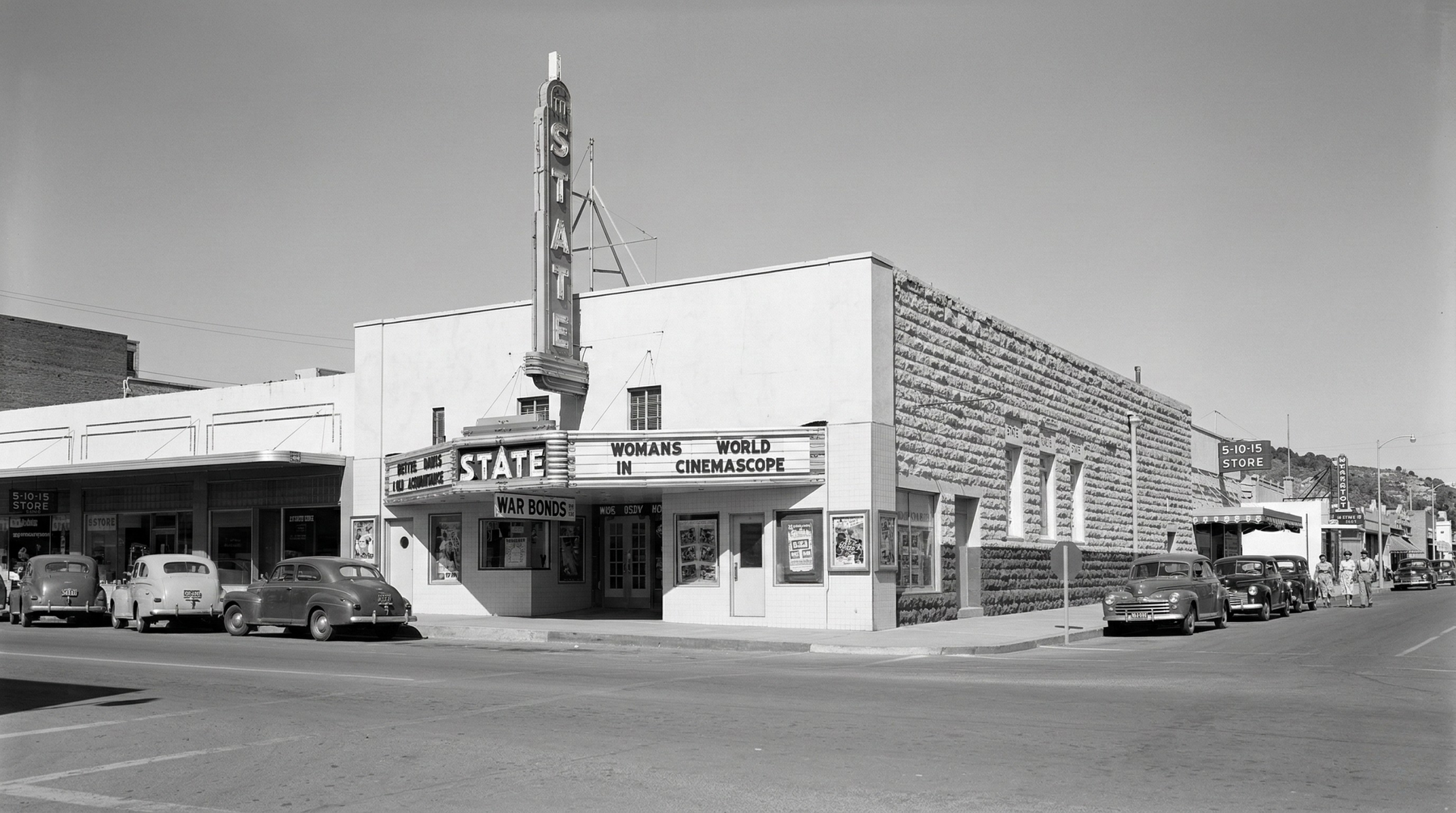 A black-and-white street-level shot of the State Theatre with vintage cars parked in front along a paved road.