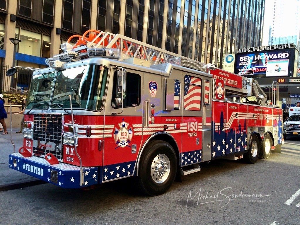Ein roter Feuerwehrtruck mit großer Leiter der New Yorker Feuerwehr fährt gerade mit Blaulicht zu einen Einsatz in Manhattan.
