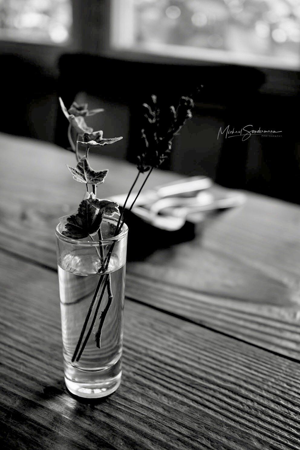 Ein Glas mit einer Rose steht auf dem Holztisch in schwarz weiss Optik.