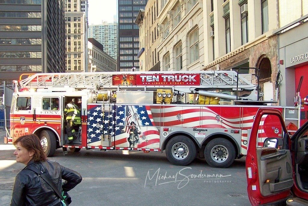 Ein roter Feuerwehrtruck mit großer Leiter der New Yorker Feuerwehr fährt gerade mit Blaulicht zu einen Einsatz in Manhattan.