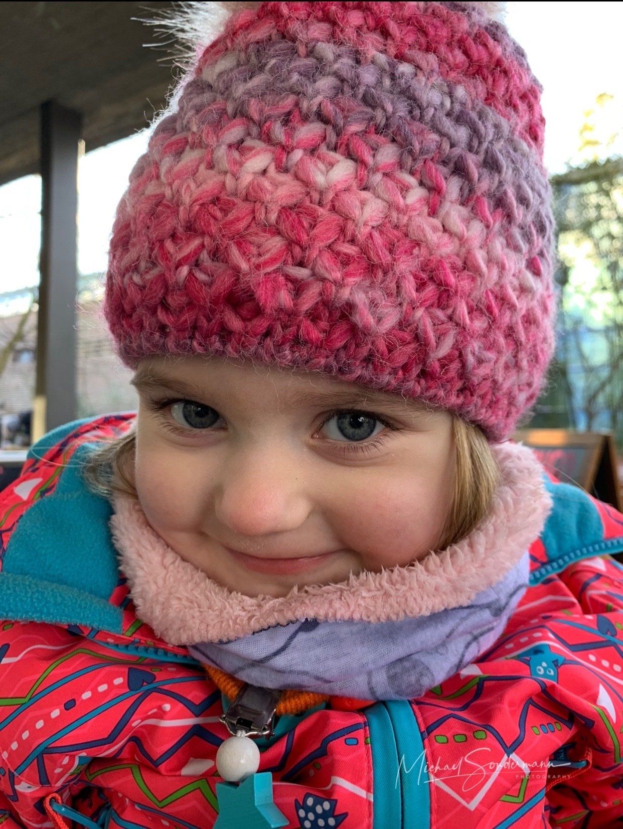 Ein junges Mädchen lächelt im Winter mit Jacke und gestrickter Mütze in die Kamera.